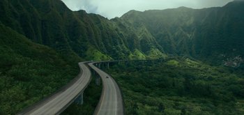 Movie still from “Triple Frontier” (2019), directed by J.C. Chandor – An aerial view of a highway going through a lush green forest; Extreme Wide shot, High angle