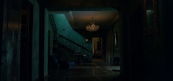 Movie still from “Triple Frontier” (2019), directed by J.C. Chandor – A chandelier hangs above a staircase in a dark room; Wide shot, High angle