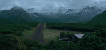 Movie still from “Triple Frontier” (2019), directed by J.C. Chandor – A dirt road going through a lush green field; Extreme Wide shot, High angle