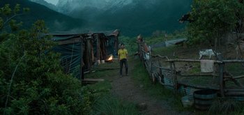 Movie still from “Triple Frontier” (2019), directed by J.C. Chandor – A man standing on a dirt path in front of a shack; Extreme Wide shot, Low angle