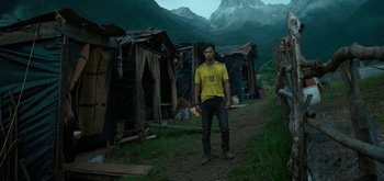 Movie still from “Triple Frontier” (2019), directed by J.C. Chandor – A man in a yellow shirt standing on a dirt road; Wide shot, Low angle