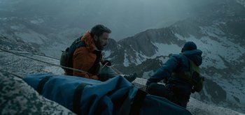 Movie still from “Triple Frontier” (2019), directed by J.C. Chandor – A man sitting on top of a mountain with a rope; Wide shot, Low angle