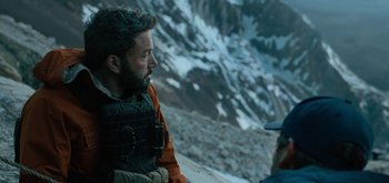 Movie still from “Triple Frontier” (2019), directed by J.C. Chandor – A man with a beard is sitting on a mountain; Medium shot, Over the shoulder angle