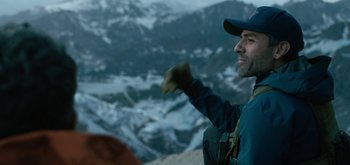 Movie still from “Triple Frontier” (2019), directed by J.C. Chandor – A man standing on top of a mountain holding a glove; Medium shot, Over the shoulder angle