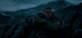 Movie still from “Triple Frontier” (2019), directed by J.C. Chandor – A man with a backpack is sitting on a hill; Medium shot, High angle