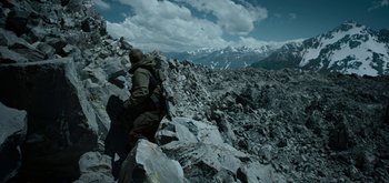 Movie still from “Triple Frontier” (2019), directed by J.C. Chandor – A man with a back pack climbing up a rocky hill; Wide shot, High angle