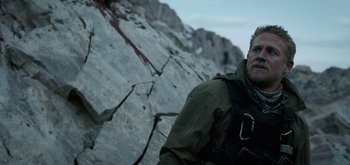 Movie still from “Triple Frontier” (2019), directed by J.C. Chandor – A man standing next to a large rock wall; Close Up shot, Over the shoulder angle