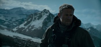 Movie still from “Triple Frontier” (2019), directed by J.C. Chandor – A person wearing a jacket near a mountain; Close Up shot, Over the shoulder angle