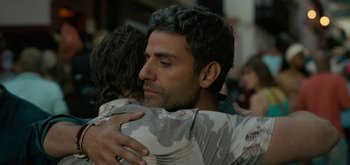 Movie still from “Triple Frontier” (2019), directed by J.C. Chandor – A man and a woman hugging each other in front of a group of people; Close Up shot, Over the shoulder angle