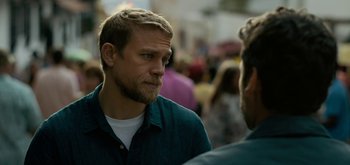 Movie still from “Triple Frontier” (2019), directed by J.C. Chandor – A man with a beard is talking to another man in a crowd of onlookers; Close Up shot, Over the shoulder angle
