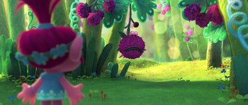 Movie still from “Trolls” (2016), directed by Mike Mitchell – A purple creature hanging from a tree in a forest; Wide shot, Low angle