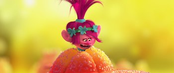 A pink haired troll is sitting on a flower