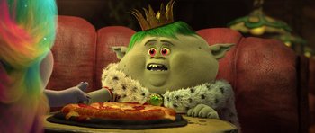 Movie still from “Trolls” (2016), directed by Mike Mitchell – A troll with a crown on his head sitting in front of a pizza; Medium shot, High angle