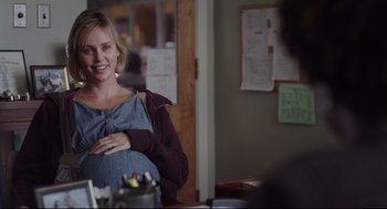 Movie still from “Tully” (2018), directed by Jason Reitman – A pregnant woman smiling at the camera in front of a mirror; Medium shot, Over the shoulder angle