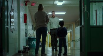 Movie still from “Tully” (2018), directed by Jason Reitman – A man and a woman and a child are standing in a school hallway; Wide shot, Low angle