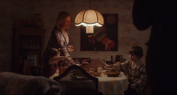 Movie still from “Tully” (2018), directed by Jason Reitman – A woman standing at a dinner table with a child; Medium shot, Over the shoulder angle