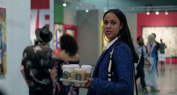 Movie still from “Velvet Buzzsaw” (2019), directed by Dan Gilroy – A woman holding a tray of drinks in her hand; Medium shot, Over the shoulder angle