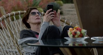Movie still from “Velvet Buzzsaw” (2019), directed by Dan Gilroy – A woman sitting in a chair looking at her cell phone; Medium shot, High angle