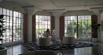 Movie still from “Velvet Buzzsaw” (2019), directed by Dan Gilroy – A woman sitting on a chair in front of a large window; Wide shot, High angle