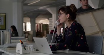 Movie still from “Velvet Buzzsaw” (2019), directed by Dan Gilroy – A woman sitting in front of an open laptop computer talking on the phone; Medium shot, Over the shoulder angle
