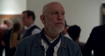 Movie still from “Velvet Buzzsaw” (2019), directed by Dan Gilroy – An older man wearing a tie and a blue jacket; Close Up shot, Over the shoulder angle