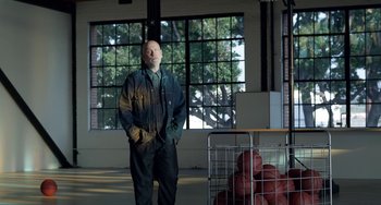 Movie still from “Velvet Buzzsaw” (2019), directed by Dan Gilroy – A man standing next to a basket full of basketballs; Wide shot, Low angle