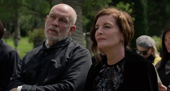 Movie still from “Velvet Buzzsaw” (2019), directed by Dan Gilroy – A man and a woman sitting next to each other in front of trees; Close Up shot, Over the shoulder angle