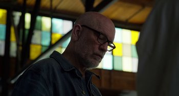 Movie still from “Velvet Buzzsaw” (2019), directed by Dan Gilroy – A bald man with glasses is looking down at the ceiling; Close Up shot, Low angle