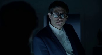 Movie still from “Velvet Buzzsaw” (2019), directed by Dan Gilroy – A man in a suit and glasses is looking at the camera; Close Up shot, Over the shoulder angle