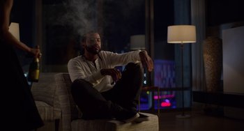 Movie still from “Velvet Buzzsaw” (2019), directed by Dan Gilroy – A man sitting on top of a chair in a living room; Medium shot, Low angle