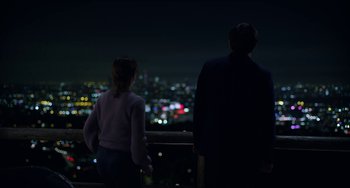 Movie still from “Velvet Buzzsaw” (2019), directed by Dan Gilroy – A man and a woman looking out over a city at night; Medium shot, Over the shoulder angle