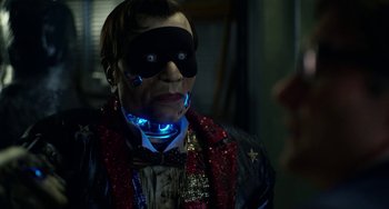 Movie still from “Velvet Buzzsaw” (2019), directed by Dan Gilroy – A man wearing a mask and a red jacket with blue lights around his neck; Close Up shot, Over the shoulder angle