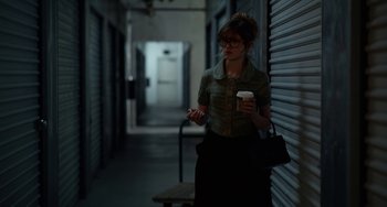 Movie still from “Velvet Buzzsaw” (2019), directed by Dan Gilroy – A woman holding a cup of coffee while standing in a hallway; Medium shot, Over the shoulder angle