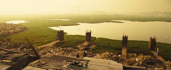 Movie still from “Slumdog Millionaire” (2008), directed by Danny Boyle – A view of a body of water with a couple of people sitting on the ground; Extreme Wide shot, High angle