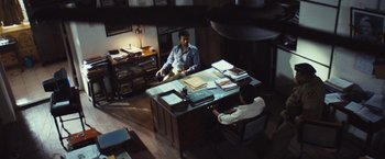 Movie still from “Slumdog Millionaire” (2008), directed by Danny Boyle – Two people sitting at a desk in a room; Wide shot, High angle