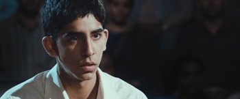 Movie still from “Slumdog Millionaire” (2008), directed by Danny Boyle – A young man in a white shirt looking at the camera; Close Up shot, Over the shoulder angle