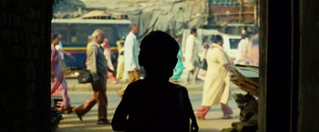 Movie still from “Slumdog Millionaire” (2008), directed by Danny Boyle – A young child standing in front of a group of people; Medium shot, Over the shoulder angle