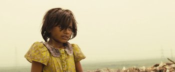Movie still from “Slumdog Millionaire” (2008), directed by Danny Boyle – A little girl in a yellow dress is standing in a field; Close Up shot, Low angle