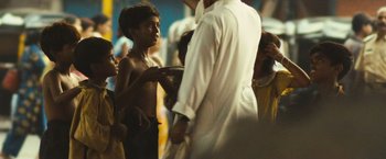 Movie still from “Slumdog Millionaire” (2008), directed by Danny Boyle – A group of people standing around a man holding a plate; Medium shot, Over the shoulder angle