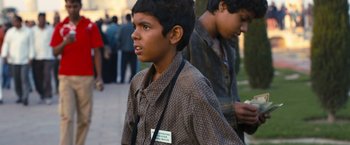 Movie still from “Slumdog Millionaire” (2008), directed by Danny Boyle – Two young boys walking down a sidewalk in front of a group of people; Medium shot, High angle