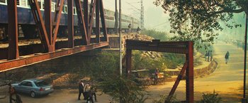 Movie still from “Slumdog Millionaire” (2008), directed by Danny Boyle – A train is crossing a bridge over a river; Extreme Wide shot, High angle