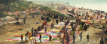 Movie still from “Slumdog Millionaire” (2008), directed by Danny Boyle – Many people are on the beach near the water; Extreme Wide shot, High angle