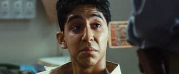 Movie still from “Slumdog Millionaire” (2008), directed by Danny Boyle – A young man looking at the camera with a sad look on his face; Close Up shot, Over the shoulder angle