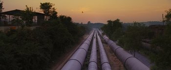 Movie still from “Slumdog Millionaire” (2008), directed by Danny Boyle – A bunch of pipes that are sitting in the grass; Extreme Wide shot, High angle