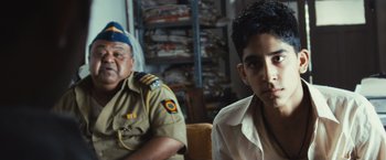 Movie still from “Slumdog Millionaire” (2008), directed by Danny Boyle – A man sitting next to another man in a room; Close Up shot, High angle