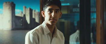 Movie still from “Slumdog Millionaire” (2008), directed by Danny Boyle – A young man wearing a white shirt is posing for a picture; Close Up shot, Low angle