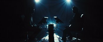 Movie still from “Slumdog Millionaire” (2008), directed by Danny Boyle – Two men sitting in front of each other holding guns in their hands; Wide shot, Low angle