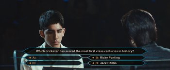 Movie still from “Slumdog Millionaire” (2008), directed by Danny Boyle – A man is playing a video game with a question mark next to him; Close Up shot, High angle