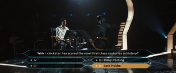 Movie still from “Slumdog Millionaire” (2008), directed by Danny Boyle – Two men sitting in front of each other in front of a microphone; Wide shot, High angle