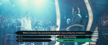 Movie still from “Slumdog Millionaire” (2008), directed by Danny Boyle – A man sitting in front of a microphone in front of a crowd; Medium shot, High angle